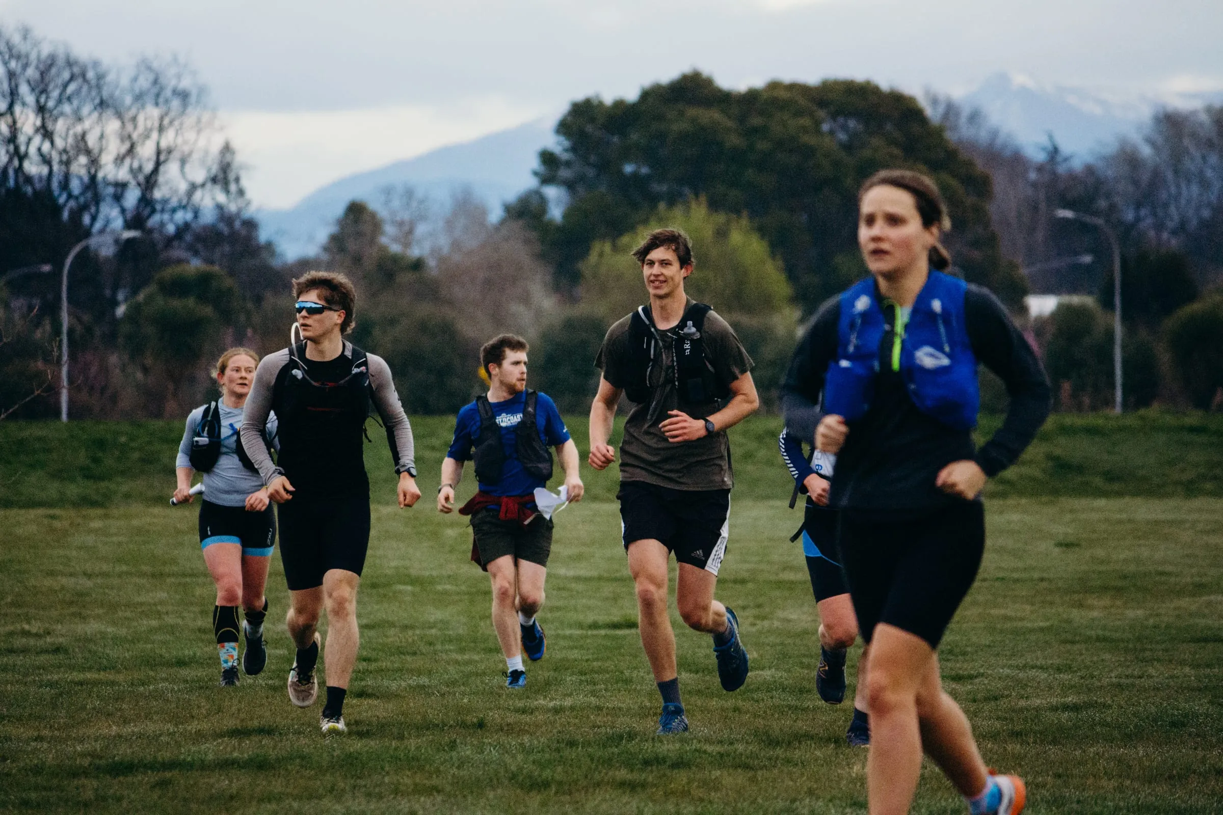Five racers running across open grass with the Southern Alps behind them