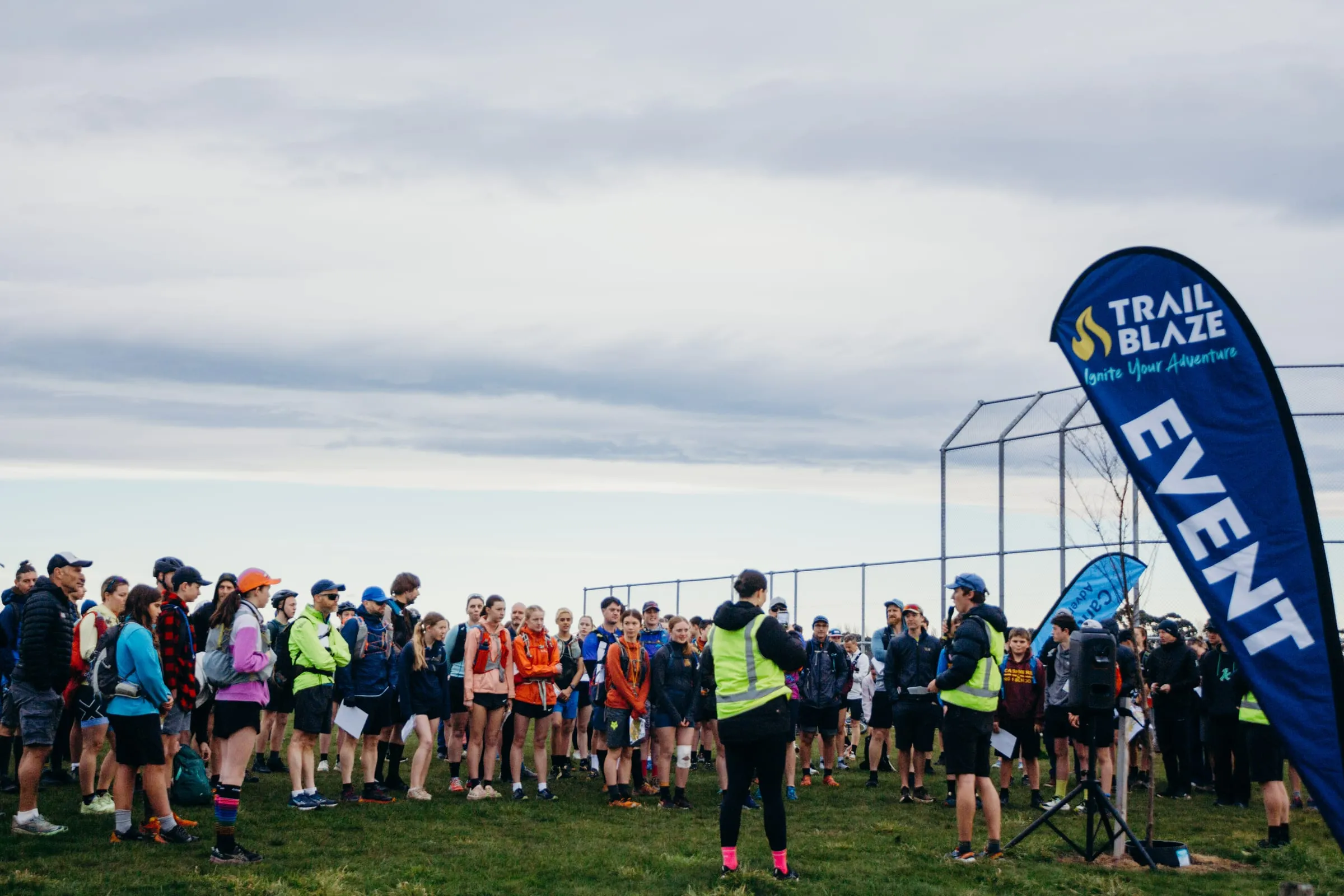 A crew member briefing a full field of adventure racers beside a TrailBlaze event flag