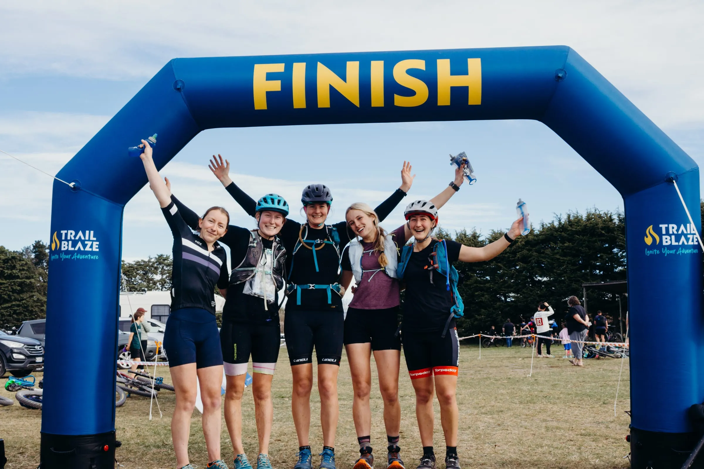 A team of five with their arms in the air under the TrailBlaze finish arch