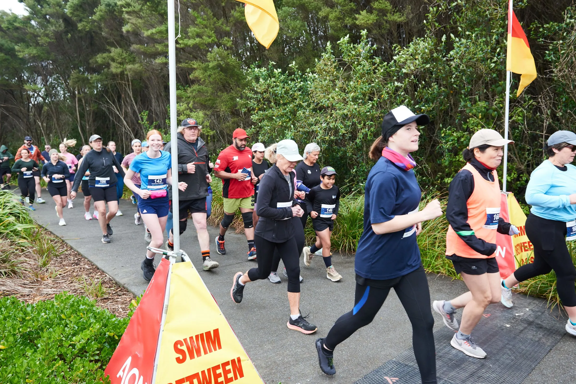 Runners stream past the surf lifesaving flags at the start of the Kahawai Point Coastal Classic