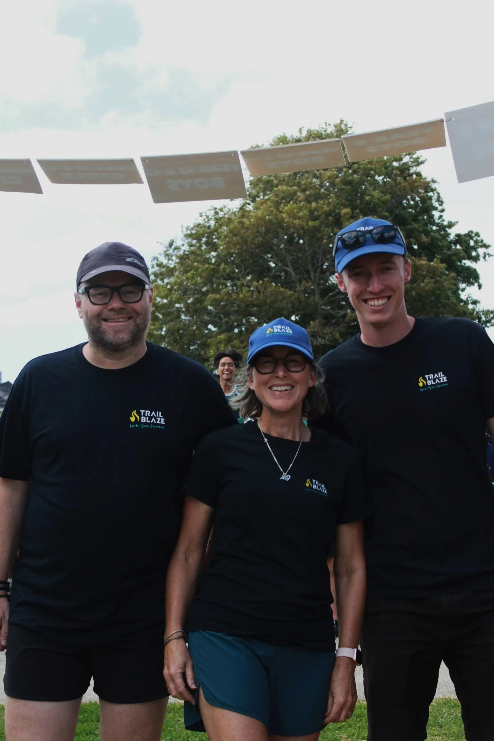 Neill, Debbie, and Callum in TrailBlaze shirts under the finish banner at a Sprint Series event